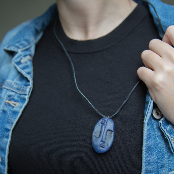 Dark blue two faced pendant inspired by African tribal masks on girl who is wearing black shirt and blue jeans jacket