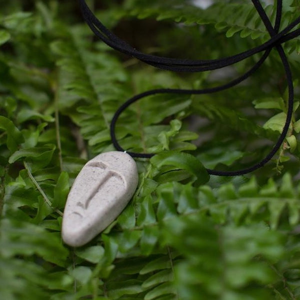 Beige colour tribal mask pendant in green fern background 