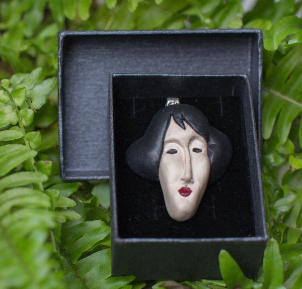 Handmade face shape pendant in black gift box photographed in green fern background