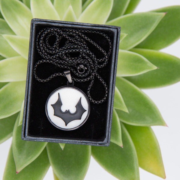 black cabochon necklace with stylised bat logo in black gift box and green background
