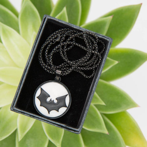 White black round necklace with batman logo sign in Green succulent background