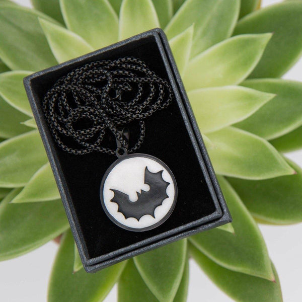 black cabochon necklace with stylised bat logo in black gift box and green background