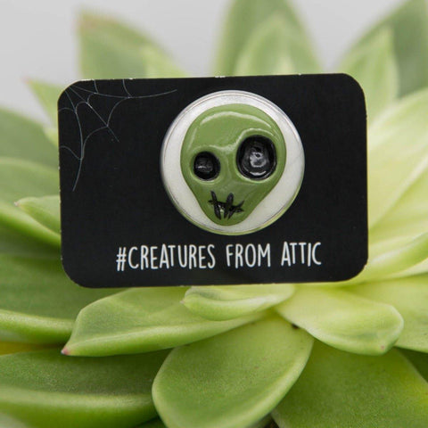 Funny hand-sculpted green alien head on white cabochon pin with label "creatures from attic" in green background