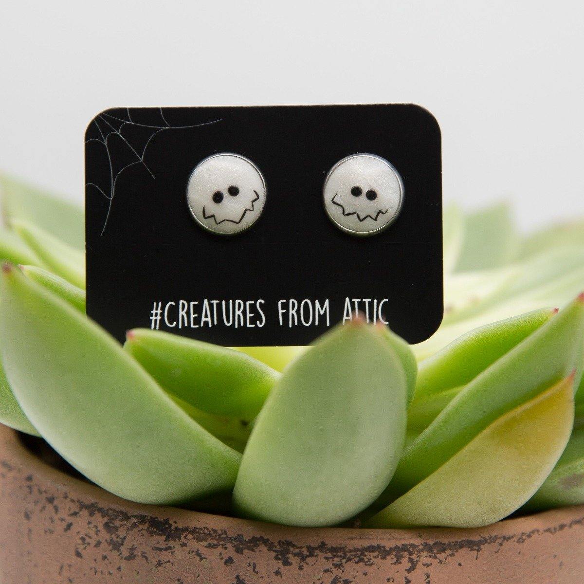 White hand-sculpted earrings with funny smile on black label named #creaturesfromattic