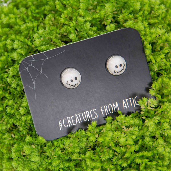a pair of white stud earrings with emoji like eyes and smile placed on green background