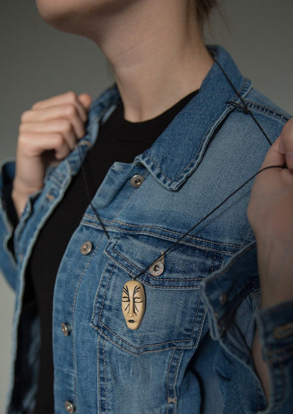 Girl demonstrating light brown stylised face pendant (black lips and black lines imitating tattoo) on blue jeans jacket  