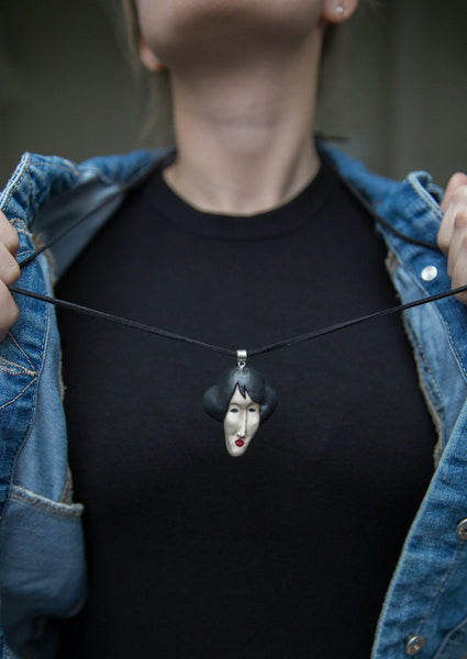 Polymer clay face pendant on leather strap and girl with black shirt and blue jeans jacket wearing it 