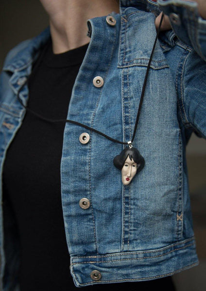Cropped photo of a woman demonstrating handmade face pendant on blue jeans jacket
