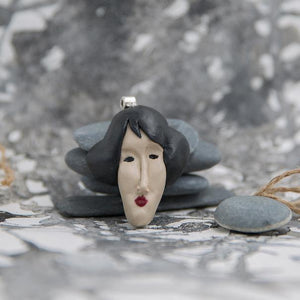 Handmade polymer clay pendant sculpted like woman's face from Modigliani's paintings photographed in grey neutral background