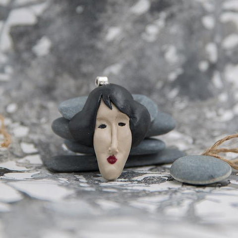 Handmade polymer clay pendant sculpted like woman's face from Modigliani's paintings photographed in grey neutral background