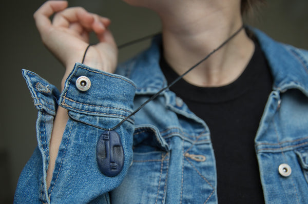 Unseen polymer clay charm inspired by tribal masks on girl with blue jacket 