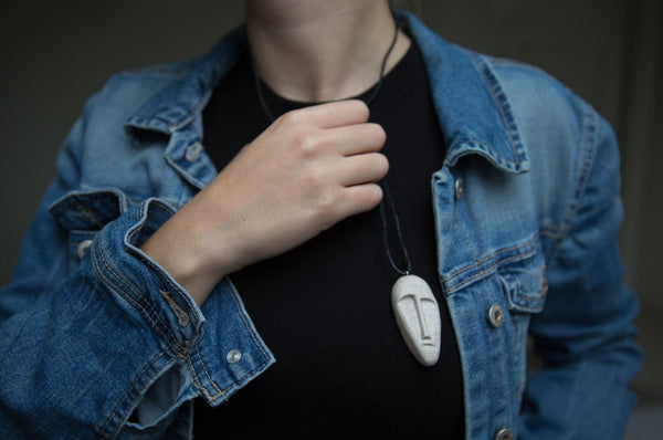 Stone mask pendant with black leather strap demonstrated on girl wearing black shirt and blue jeans jacket