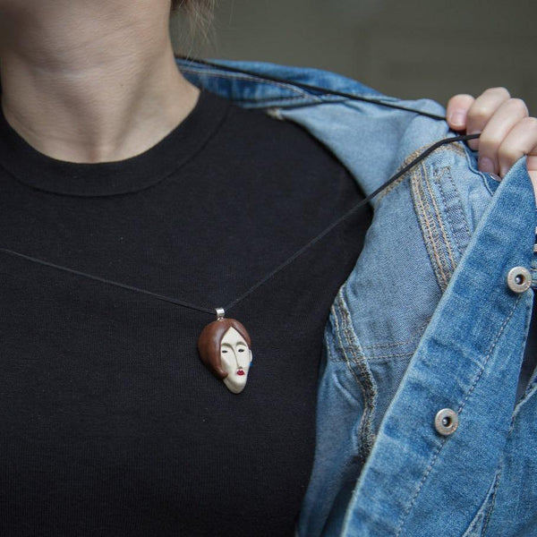 Cropped photo of a woman demonstrating handmade face pendant on black shirt and blue jeans jacket
