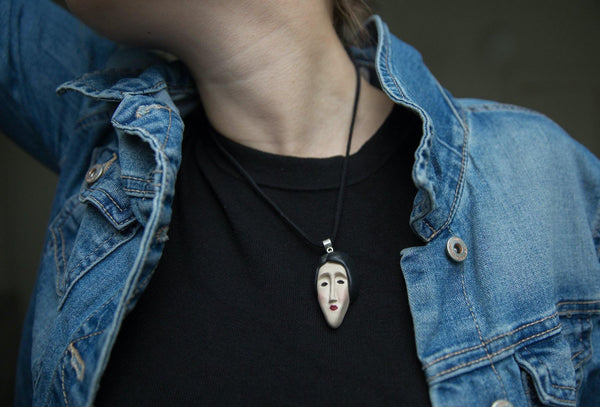 Cropped photo of girl demonstrating how face pendant looks like on black t-shirt and jeans jacket